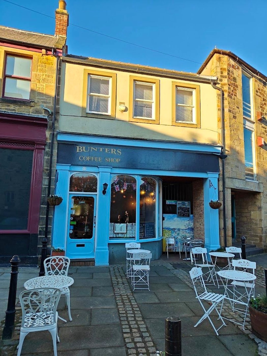 The blue-painted front of Bunters Coffee Shop on Hallgate, with white iron tables and chairs on the pavement outside